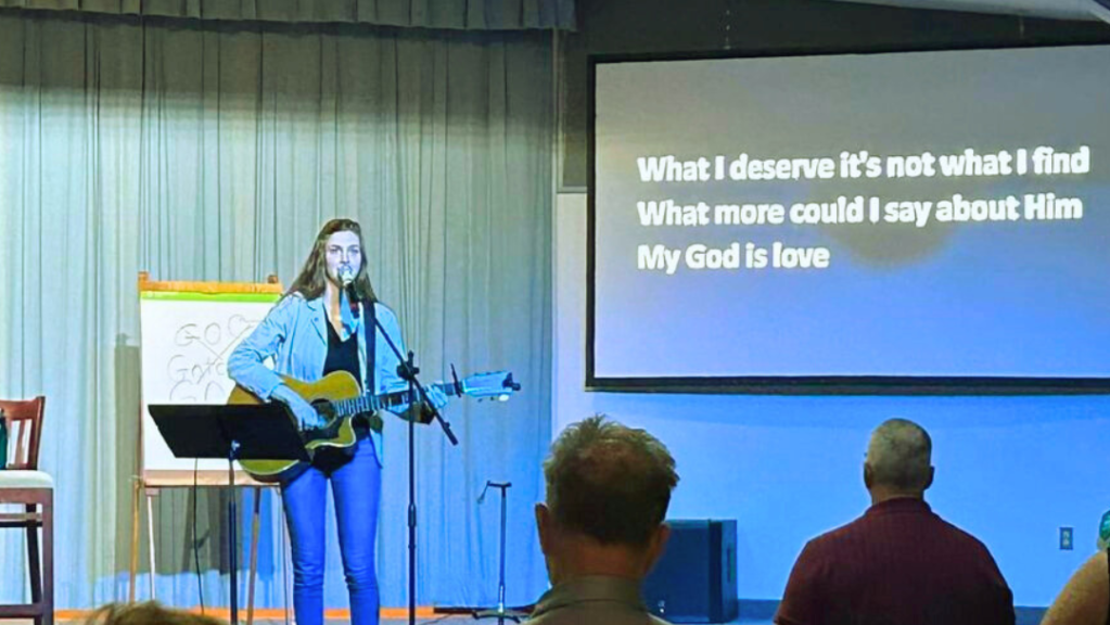 image of Chase Meahl standing on stage leading worship with a guitar in her hands.